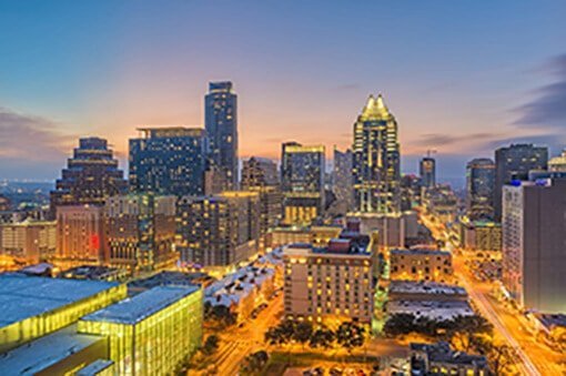 The city of Austin at dusk, lit up in front of a sunset sky, near where Austin Landmark Property Services provides Austin property management.